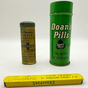 May include: Three vintage metal containers: one green with "Doan's Pills" text, one yellow and gold with "Dr. Edwards' Olive Tablets" text, and one yellow with "Fineline Sheaffer's" text. The containers are cylindrical and rectangular.