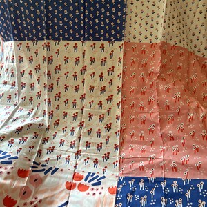 May include: A textile fabric featuring a patchwork design of various floral and abstract patterns. The color palette includes navy blue, cream, and soft pink, with repeating motifs of small flowers, red tulip-like shapes, and blue brushstrokes.