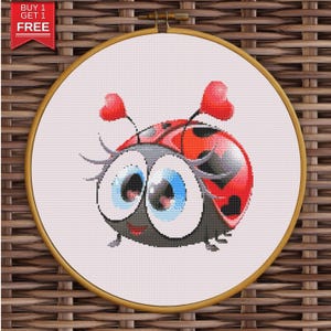 Può includere: Ricamo a punto croce di una coccinella dei cartoni animati con grandi occhi blu, antenne a forma di cuore rosse e un guscio rosso e nero. Il ricamo è ambientato in un telaio di legno su uno sfondo tessuto. Il testo "BUY 1 GET 1 FREE" è in alto a sinistra.