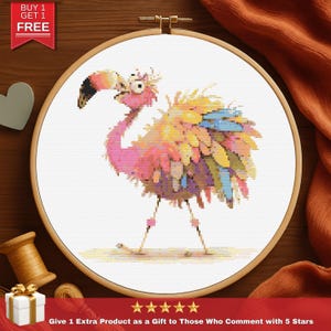 May include: A cross-stitch embroidery of a flamingo in a wooden hoop. The flamingo is pink, yellow, and blue with a black beak. The text "BUY 1 GET 1 FREE" is in the upper left corner. The text "Give 1 Extra Product as a Gift to Those Who Comment with 5 Stars" is at the bottom.