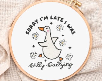 May include: A cross-stitch embroidery hoop featuring a white goose with an orange beak and feet, surrounded by daisies and stars. The text reads "Sorry I'm late, I was dilly dallying" in black lettering. The hoop is made of wood.