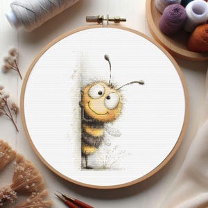 May include: Cross-stitch embroidery hoop featuring a cartoon bee design. The bee is yellow and black, peeking around a corner with a friendly expression. The embroidery hoop is made of wood and is surrounded by craft supplies.