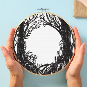 Può includere: Cerchio da ricamo in bianco e nero con un disegno di alberi che formano un cerchio attorno a uno spazio vuoto. Gli alberi sono stilizzati e hanno un aspetto fantasioso.