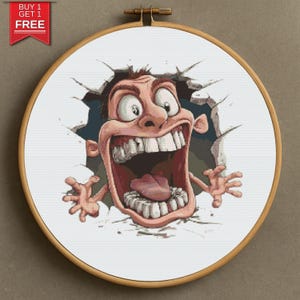 May include: A cross-stitch embroidery hoop with a cartoon character breaking through a wall. The character has a wide open mouth, large eyes, and is colored in shades of pink, brown, and white. The text "BUY 1 GET 1 FREE" is in the upper left corner.