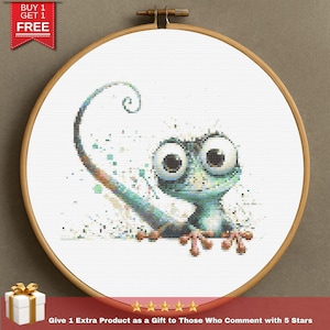 May include: Cross-stitch of a cartoon chameleon with large eyes, in a wooden embroidery hoop. The chameleon is blue and green, with a long, curled tail. The text "BUY 1 GET 1 FREE" is in the upper left corner.