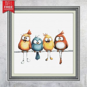May include: A framed cross-stitch featuring four cartoon birds perched on a wire. The birds are in shades of orange, yellow, and blue, with large eyes and open beaks. The frame is silver, and a "BUY 1 GET 1 FREE" banner is in the upper left corner.