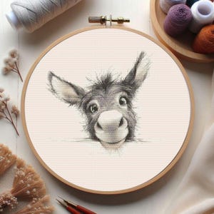 May include: Cross-stitch embroidery of a donkey's face, framed in a wooden hoop. The donkey has a gray and white color scheme with large, expressive eyes and a friendly expression. The background is a light beige fabric.