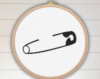 May include: A black and white embroidery hoop with a simple black safety pin design.