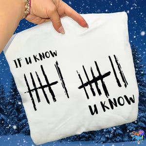 May include: White pillowcase with the text "IF U KNOW" and "U KNOW" in black, along with tally marks. The pillow is held up by a hand with a gold bracelet. The background is a winter scene.