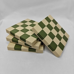 May include: Four square coasters with a green and beige chequered pattern. Each coaster has a beige base with alternating green and beige squares. The coasters are stacked and angled.