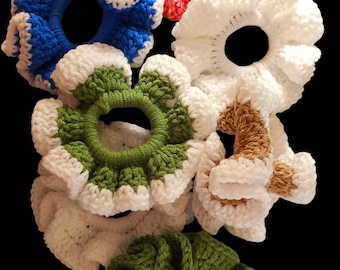 May include: Six crocheted hair scrunchies in various colors, including white, blue, green, pink, and brown. The scrunchies are all made with a ruffled design.