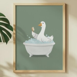 May include: A framed print featuring a white goose in a bathtub with bubbles, holding a toothbrush. The artwork has a light green background and a wooden frame. The goose has an orange beak and is surrounded by blue bubbles.