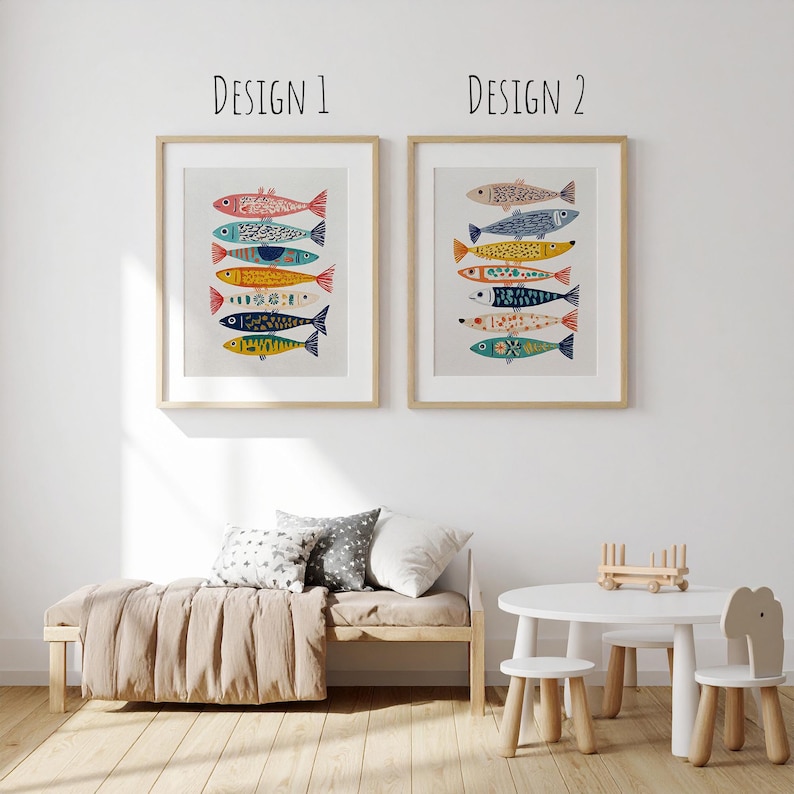 May include: Two framed art prints featuring colorful fish designs. The prints are labeled "Design 1" and "Design 2" at the top. The fish are in various colors, including red, blue, yellow, and orange, with decorative patterns. The artwork is displayed in a light-colored room.