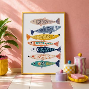 May include: A framed art print featuring seven stylized fish in various colors and patterns. The fish are arranged vertically against a white background, with a gold frame. The artwork is displayed on a pink and white tiled surface.