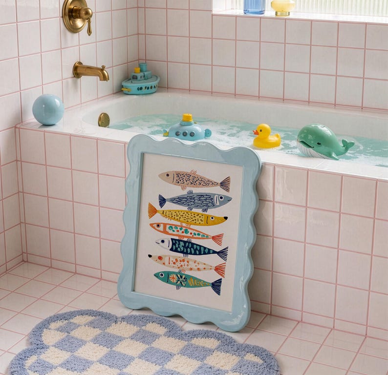 May include: A framed art print featuring colorful fish illustrations in a light blue scalloped frame. The artwork is displayed in a bathroom setting with a blue and white checkered rug, and toy boats and animals in the bathtub.