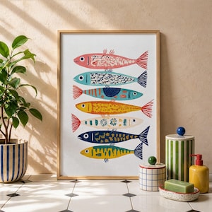 May include: A framed art print featuring a colorful illustration of seven stylized fish. Each fish has a unique pattern and color, including pink, blue, yellow, and green, with red tail fins. The artwork is displayed on a white background.