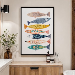 May include: A framed art print featuring six stylized fish in various colors. The fish are arranged vertically against a white background. Each fish has unique patterns and colors, including blue, yellow, and orange. The frame is black.