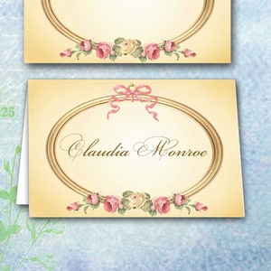 Op de afbeelding: Twee placecards met een gouden ovale lijst en roze rozen. De bovenste kaart is leeg en de onderste kaart heeft de naam "Claudia Monroe" in cursief geschreven.