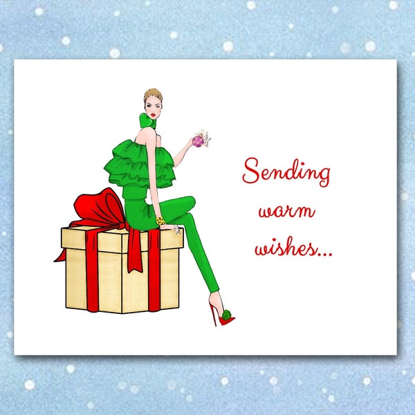 May include: Greeting card with a fashion illustration of a person in green attire sitting on a gift box with a red bow. The card reads "Sending warm wishes..." in red script against a blue background with white dots.
