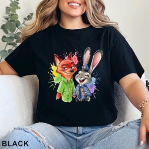 May include: Black t-shirt featuring a colorful graphic of a fox and a rabbit, with paint splatter accents. The fox wears a green shirt, and the rabbit is in a police uniform. The word "BLACK" is printed at the bottom.