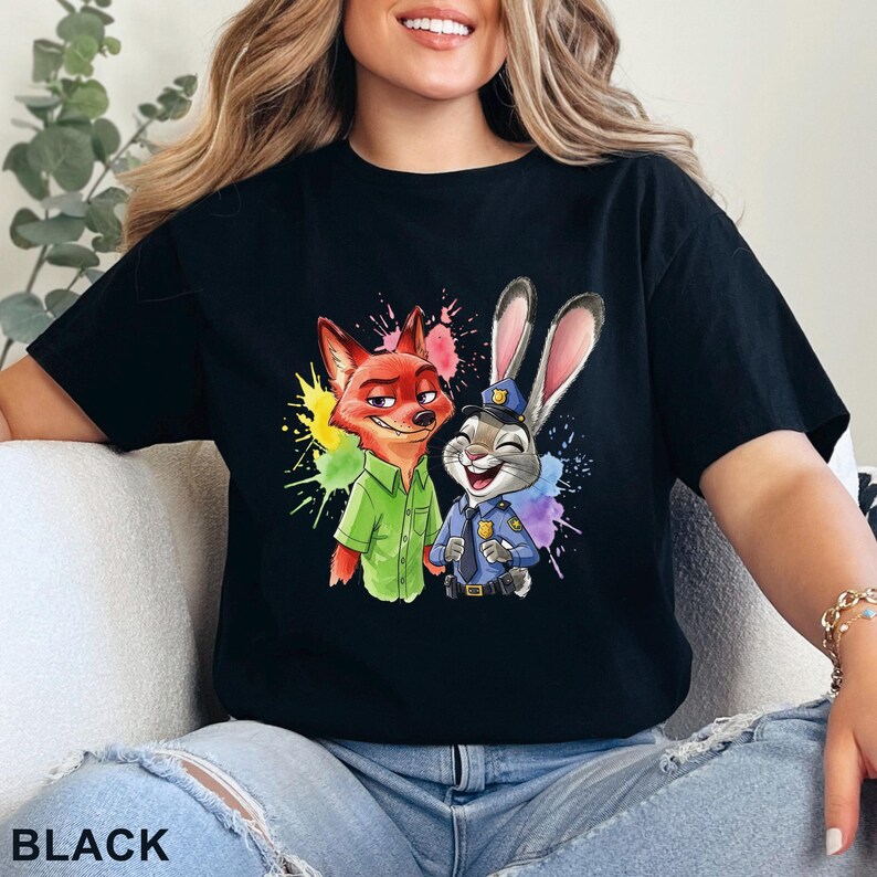 May include: Black t-shirt featuring a colorful graphic of a fox and a rabbit, with paint splatter accents. The fox wears a green shirt, and the rabbit is in a police uniform. The word "BLACK" is printed at the bottom.