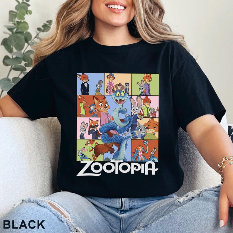 Peut inclure: T-shirt noir avec un motif color&eacute; repr&eacute;sentant des personnages du film "Zootopie". Le design comprend un renard, un lapin et d'autres animaux. Le mot "ZOOTOPIA" est imprim&eacute; en blanc.