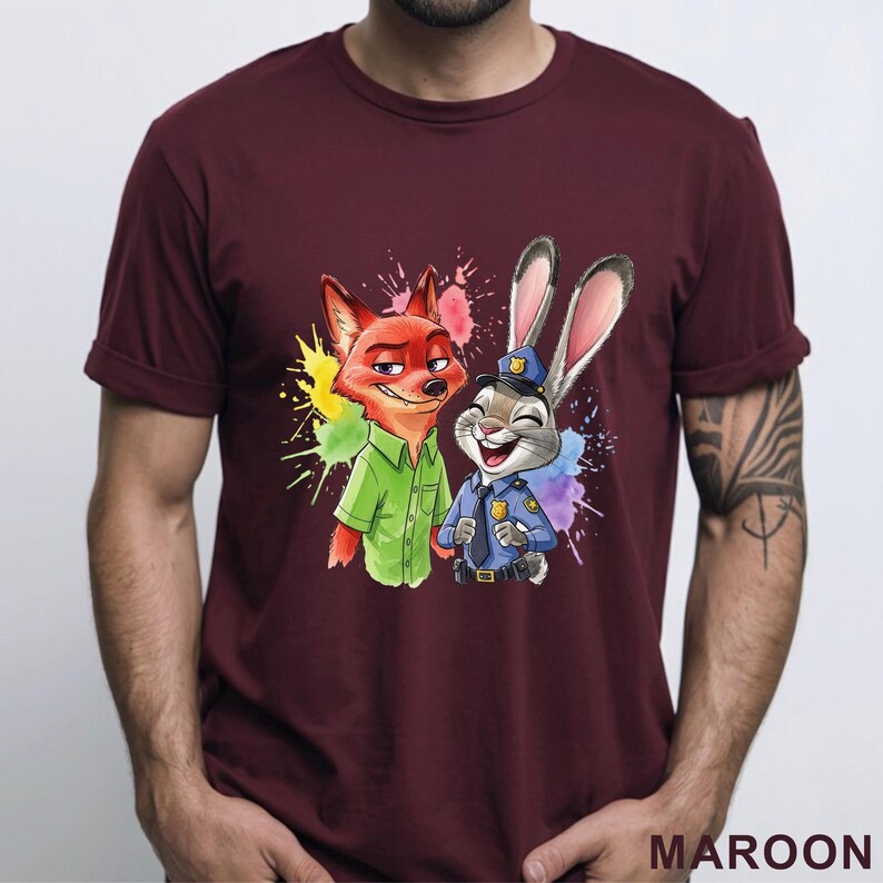 May include: Maroon t-shirt featuring a colorful graphic of a fox and a rabbit from Zootopia. The fox is wearing a green shirt, and the rabbit is in a police uniform. The design includes colorful paint splatters.