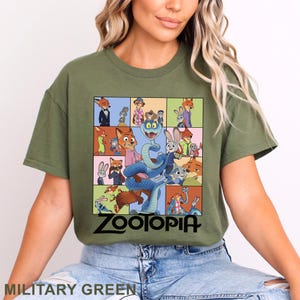 Peut inclure: T-shirt vert militaire avec un motif color&eacute; du film Zootopie. Le motif pr&eacute;sente divers personnages du film, avec le mot "Zootopia" en noir en bas. Le t-shirt est de style col rond.