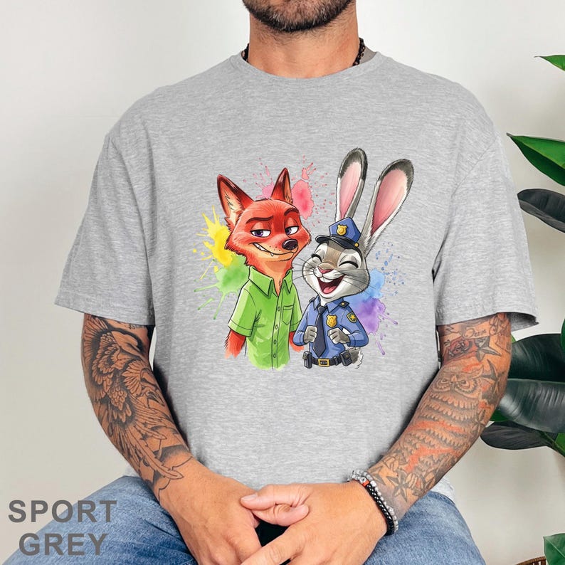 May include: Sport grey t-shirt featuring a colorful illustration of Nick Wilde the fox and Judy Hopps the rabbit from Zootopia. Nick is wearing a green shirt, and Judy is in a police uniform. The design includes colorful paint splatters.