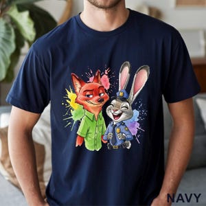May include: Navy blue t-shirt featuring a colorful graphic of Nick Wilde the fox and Judy Hopps the rabbit from Zootopia. The design includes vibrant paint splatters. The word "NAVY" is printed at the bottom right.