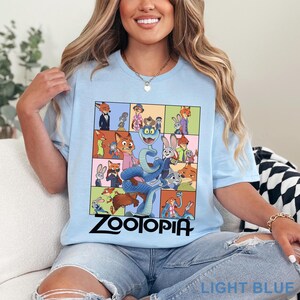 Peut inclure: T-shirt bleu clair avec un motif color&eacute; de personnages du film d'animation "Zootopie". Le motif comprend une grille d'images et le mot "Zootopia" en noir. Le t-shirt est fait d'une mati&egrave;re douce.