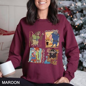 Puede incluir: Sudadera granate con un dise&ntilde;o de cuatro paneles con personajes de dibujos animados. Cada panel muestra un personaje diferente de una pel&iacute;cula, con detalles y patrones coloridos. La palabra "MAROON" est&aacute; impresa en la parte inferior.