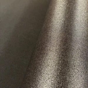 May include: A roll of dark charcoal gray fabric featuring a fine, textured weave with a subtle metallic sheen that catches the light, creating a gradient effect across the surface of the material as it curves.