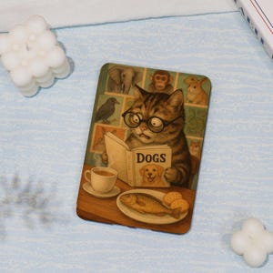 May include: A rectangular wooden coaster features a whimsical illustration of a cat wearing glasses and reading a book titled "DOGS." A cup of coffee, a plate of fish, and cookies are on the table. The background includes images of various animals.