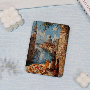 May include: A painting depicting a view from a window in Venice, Italy. The painting shows a canal with boats, a church in the distance, and a pizza and two bottles of wine on a table in the foreground.