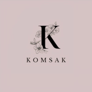 May include: A black letter "K" with floral accents, part of the word "KOMSAK", on a light pink background. The flowers are detailed with delicate lines, creating an elegant and feminine design.