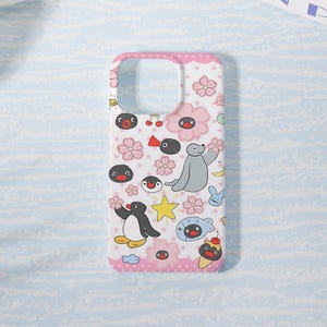 May include: A white smartphone case featuring a repeating pattern of Pingu characters, pink cherry blossoms, yellow stars, cherries, and small fish. The top and bottom edges of the case have a pink border with white polka dots.