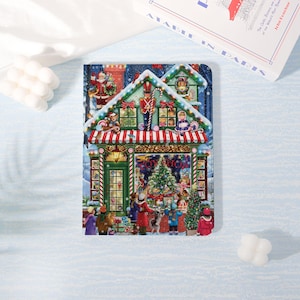 May include: A Christmas-themed notebook featuring a detailed illustration of a toy shop. The shop has a red and white striped awning, a Christmas tree, and figures of Santa Claus and a toy soldier. The text "TOY SHOP" is visible on the shop's window.