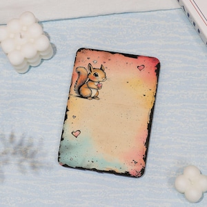 May include: A rectangular, decorative plaque featuring a cartoon squirrel holding a heart. The background has a watercolor effect with pink, yellow, and blue hues. Small hearts are scattered across the design, and the edges are dark.