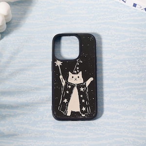 May include: A black phone case featuring a white illustration of a cat dressed as a wizard, holding a wand with a star on top. The cat wears a wizard hat and cape with star accents. The case has a dark blue border.