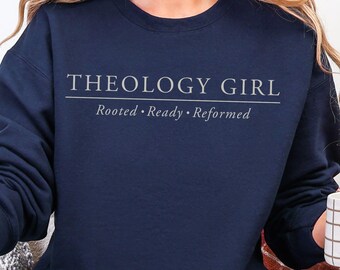 May include: A navy blue crew neck sweatshirt with the text "THEOLOGY GIRL" above the words "Rooted • Ready • Reformed" in a light grey font. The long-sleeved top is a casual style.