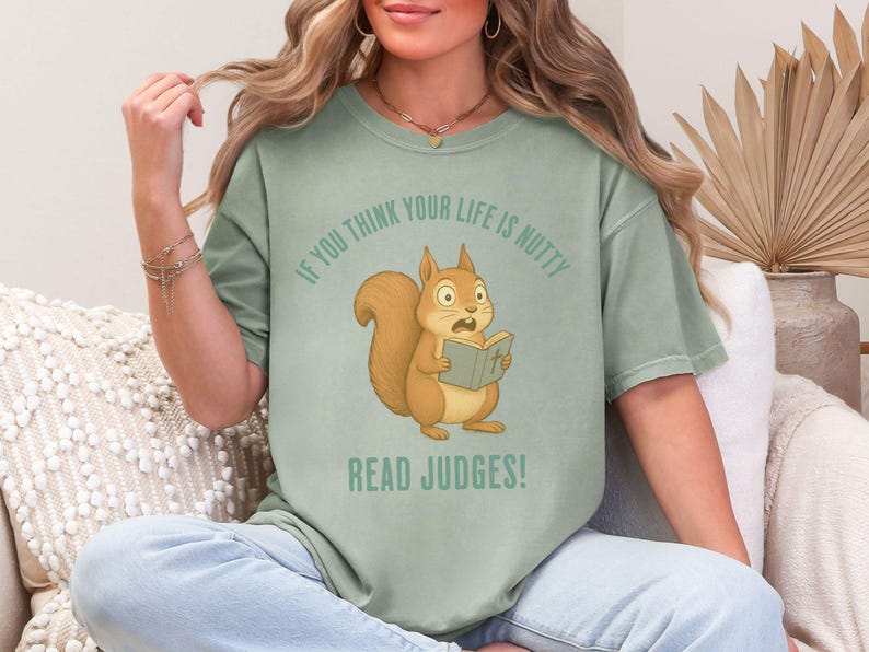 May include: Sage green t-shirt featuring a cartoon squirrel reading a book with the text "If you think your life is nutty, read Judges!". The squirrel is brown with a surprised expression. The shirt is a comfortable, casual style.
