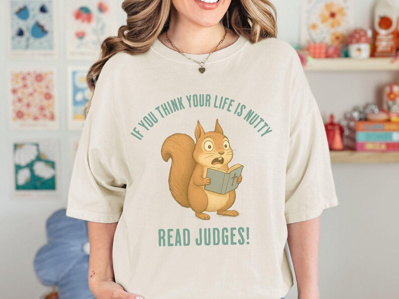 May include: Cream-colored t-shirt featuring a cartoon squirrel reading a book with the text "IF YOU THINK YOUR LIFE IS NUTTY READ JUDGES!". The squirrel is brown with a surprised expression.