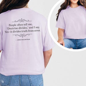Op de afbeelding: Lichtpaars T-shirt met de quote "People often tell me, 'Doctrine divides,' and I say, Yes-it divides truth from error. - JOHN MACARTHUR" op de rug. Het shirt is effen en heeft korte mouwen.