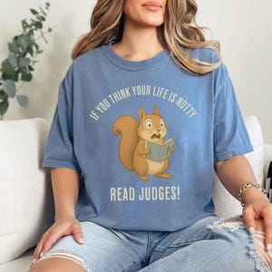 May include: A light blue t-shirt with the text "IF YOU THINK YOUR LIFE IS NUTTY READ JUDGES!" and a cartoon squirrel reading a book. The squirrel is brown with a fluffy tail and wide eyes.