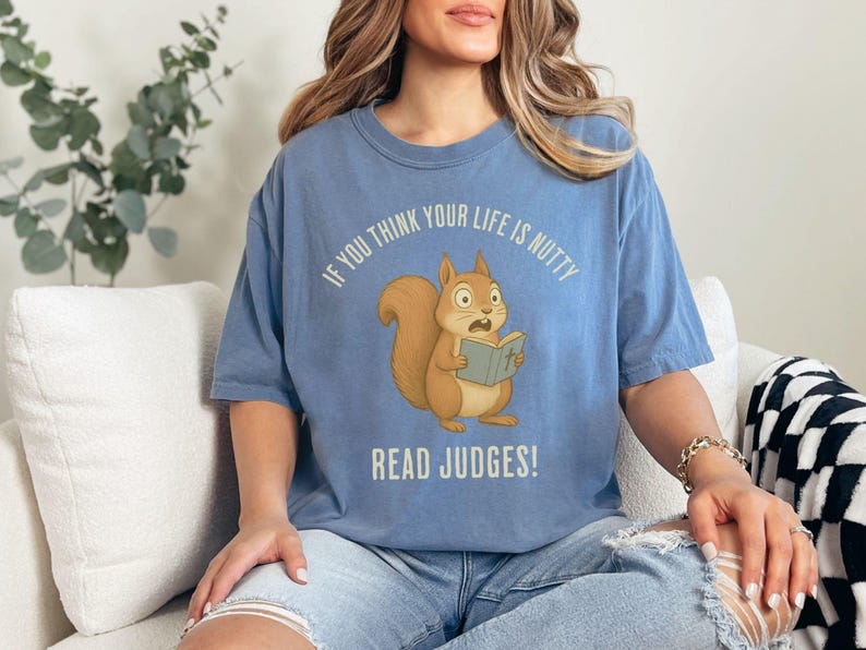 May include: A light blue t-shirt with the text "IF YOU THINK YOUR LIFE IS NUTTY READ JUDGES!" and a cartoon squirrel reading a book. The squirrel is brown with a fluffy tail and wide eyes.