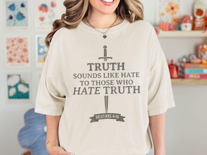 May include: Cream-colored t-shirt with the text "TRUTH SOUNDS LIKE HATE TO THOSE WHO HATE TRUTH" in gray, along with a sword graphic. The text "GALATIANS 4:16" is below the text. The shirt is a casual style.