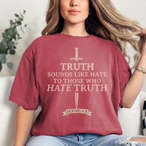 May include: A maroon t-shirt with the text "TRUTH sounds like hate to those who hate truth" in a light brown color. The shirt also features a sword and banner graphic. The text "Galatians 4:16" is printed on the banner.