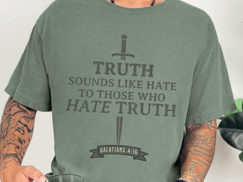 May include: Sage green t-shirt with the text "TRUTH SOUNDS LIKE HATE TO THOSE WHO HATE TRUTH" in dark gray, along with a sword graphic. The text "GALATIANS 4:16" is below the sword. The shirt is a comfortable, casual style.