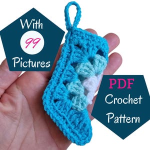 May include: A small, handmade crochet stocking in shades of blue, held in a hand. The stocking features a textured design and a loop for hanging. Text on the image reads "With 99 Pictures" and "PDF Crochet Pattern".